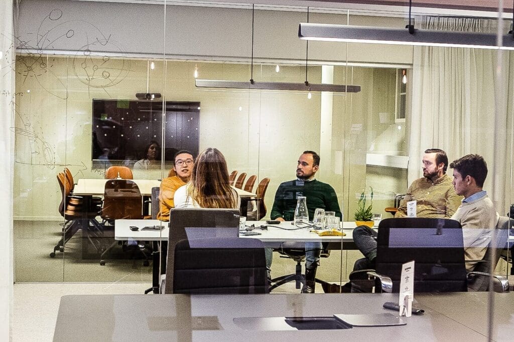 Coworkers sitting in a meeting room with glass walls curtains plant